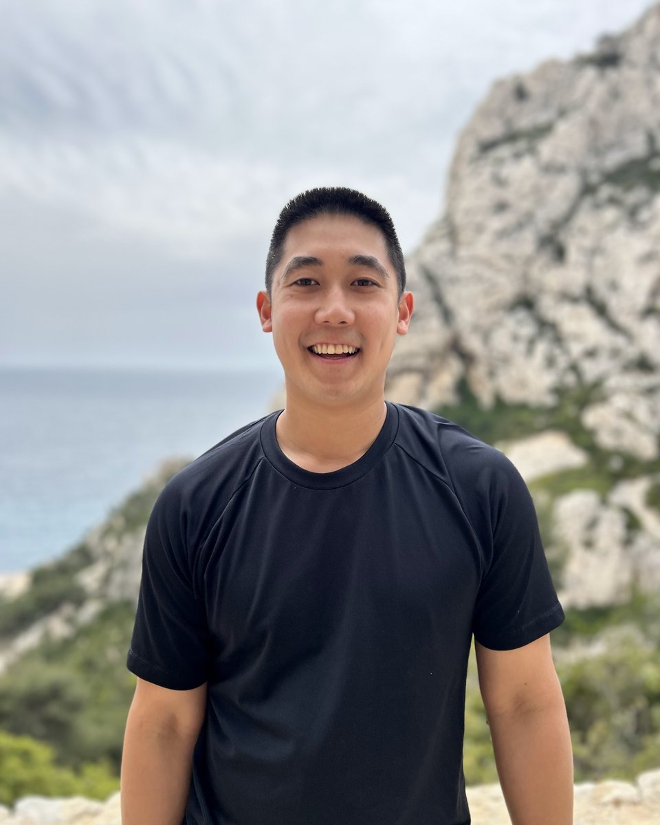 John Wu smiling on a coastal cliff trail above the sea